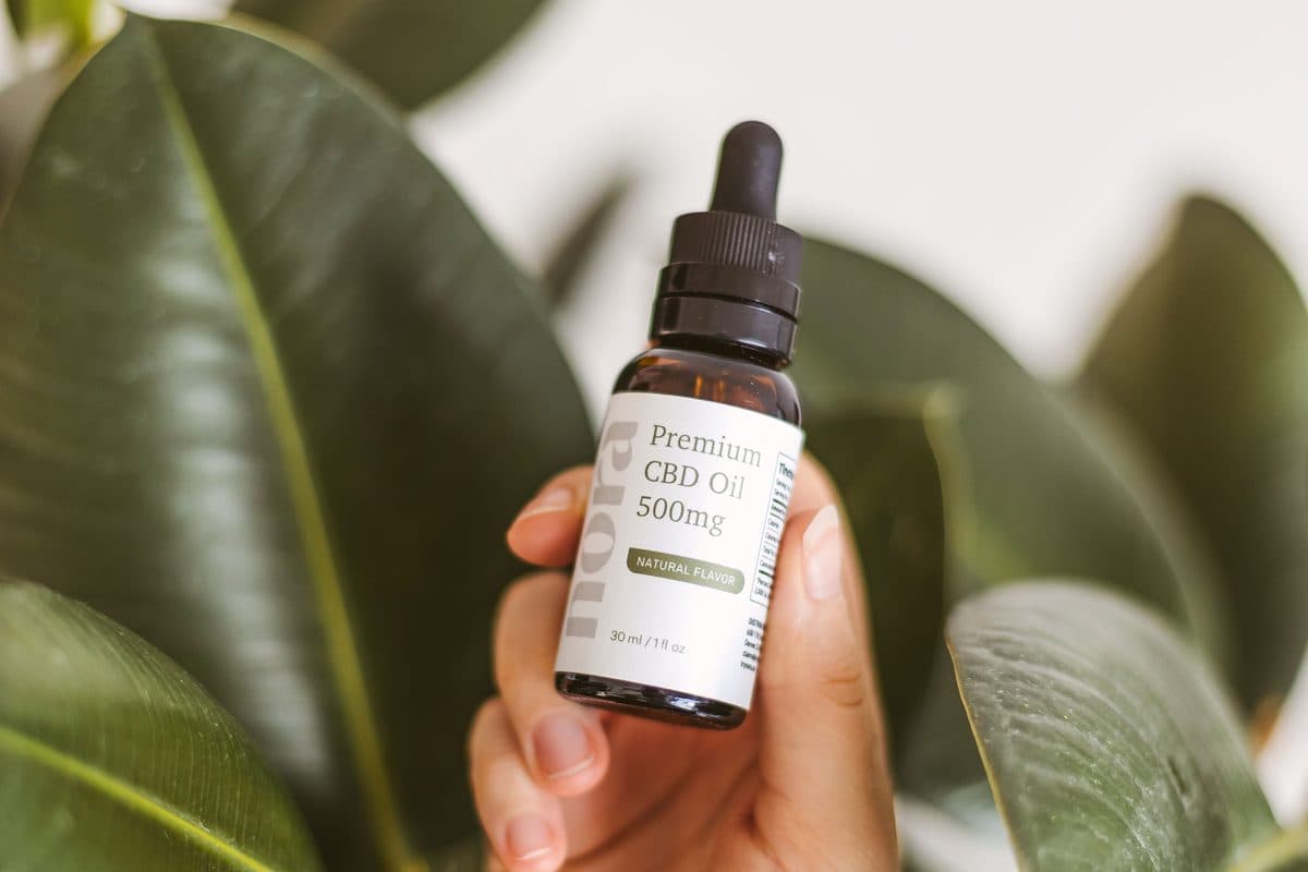 Frasco de aceite premium de cannabis CBD sostenido en mano, con hojas verdes de fondo — producción propia de HyperLeaf